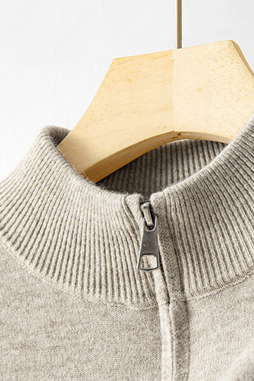 Close-up of a beige sweater with a collar and zipper on a wooden hanger against a light background.
