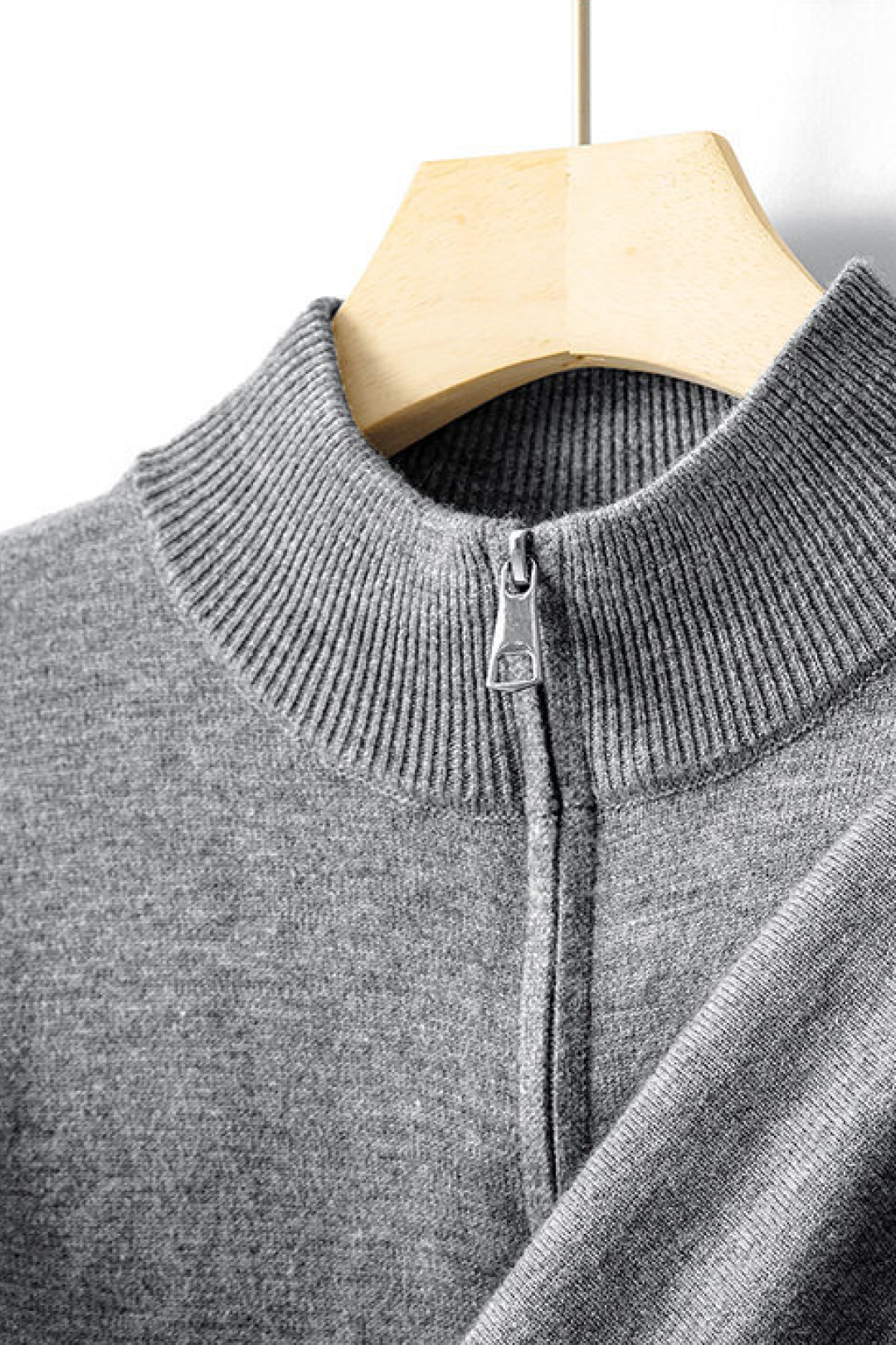 Gray sweater with a zipper on a wooden hanger against a white background