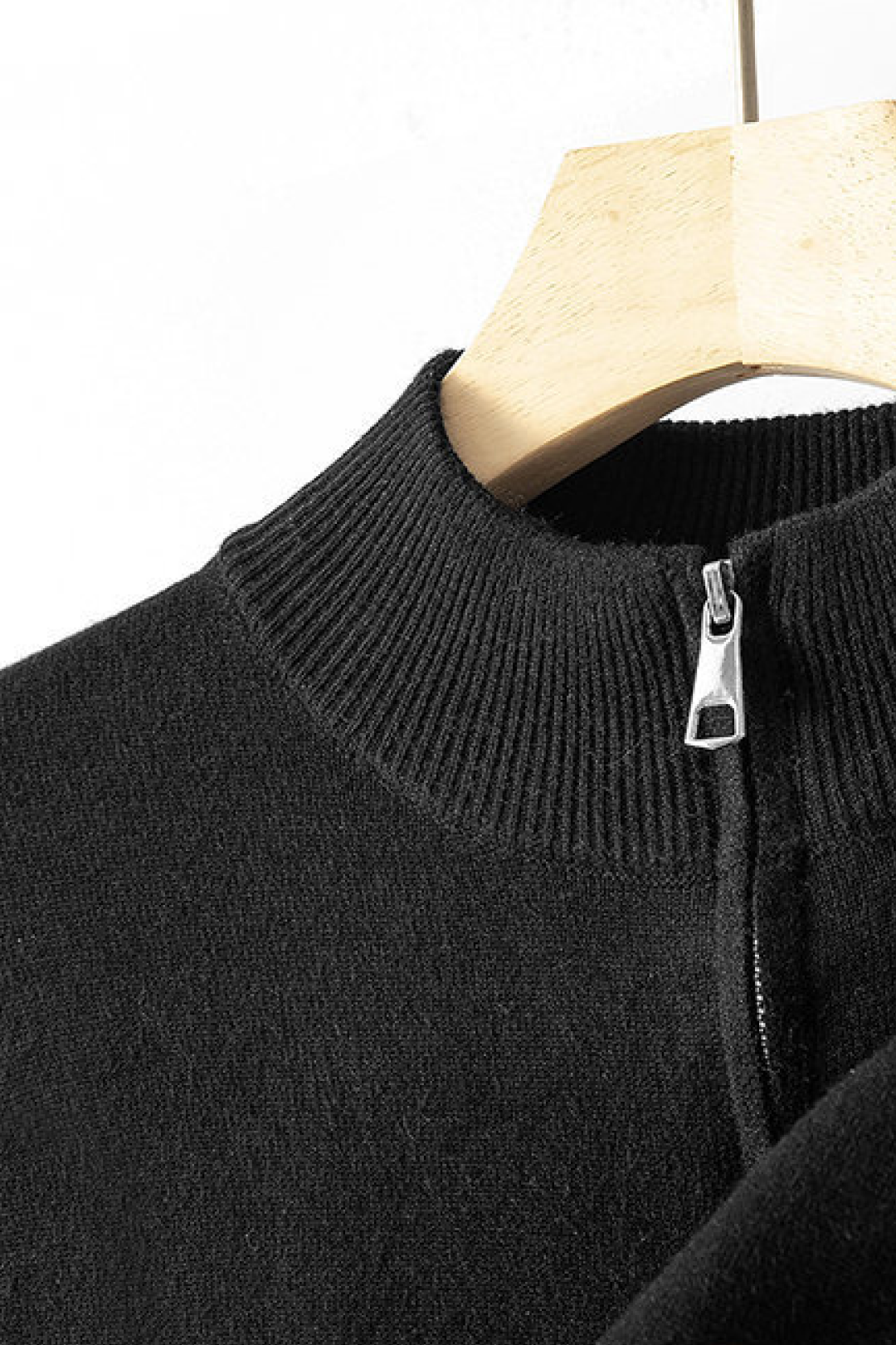 Black sweater with a zipper on a wooden hanger against a white background