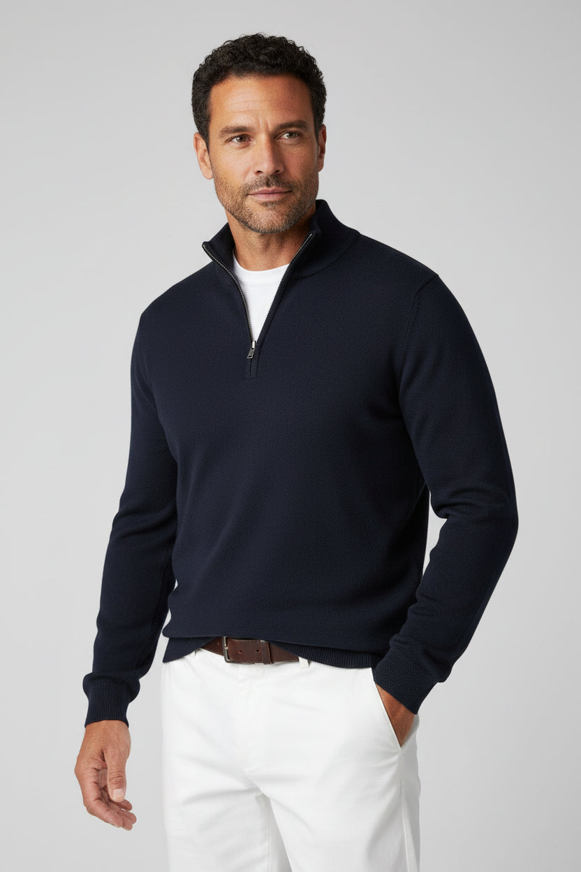 Man wearing a navy blue quarter-zip sweater and blue jeans with a blurred background