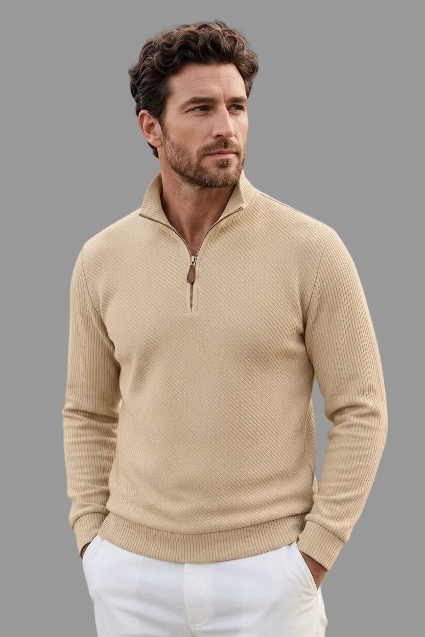 A man wearing a beige ribbed quarter-zip sweater, white pants, and black sunglasses, shown from the waist up against a plain white background.