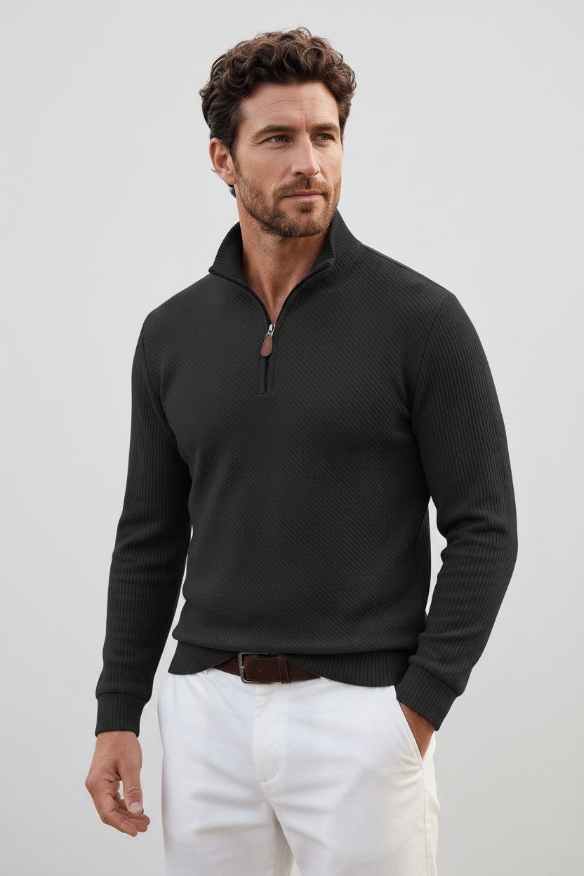 A man wearing a black textured quarter-zip pullover sweater with a stand collar, paired with white pants and black sunglasses, shown against a plain white background.