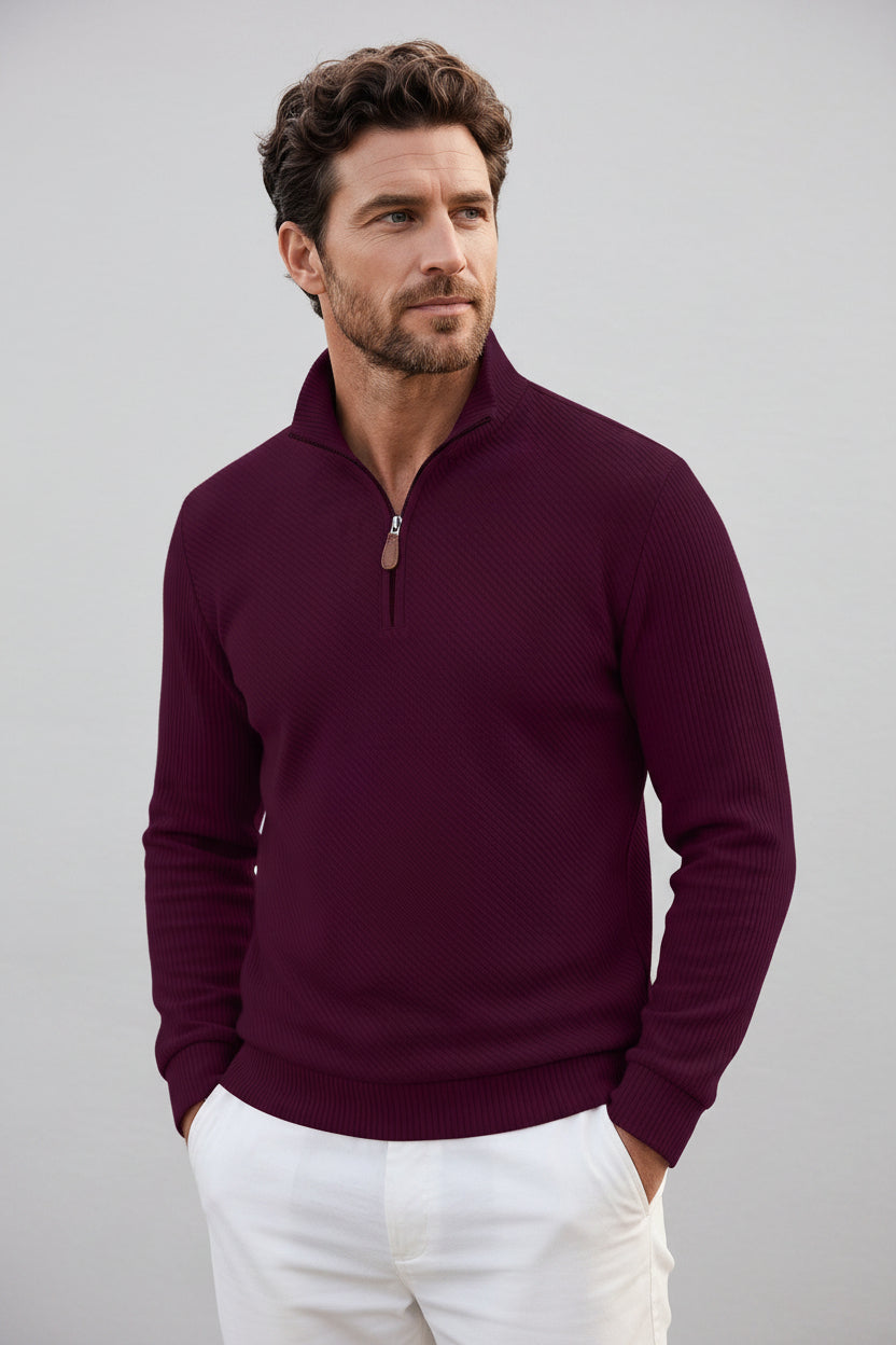 A man wearing a dark burgundy ribbed quarter-zip sweater, white pants, and black sunglasses, shown from the waist up against a plain white background.