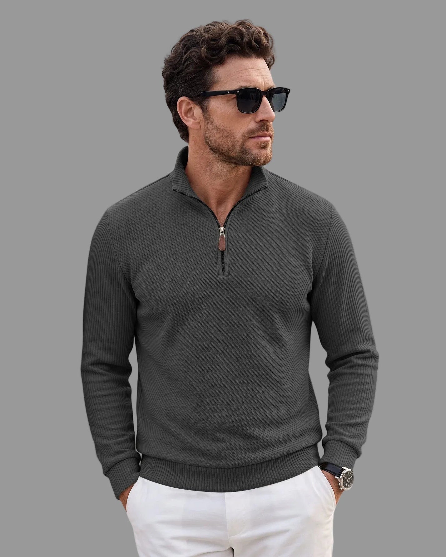 A man wearing a dark gray ribbed long-sleeve quarter-zip pullover sweater, white pants, and black sunglasses, standing against a plain white background.