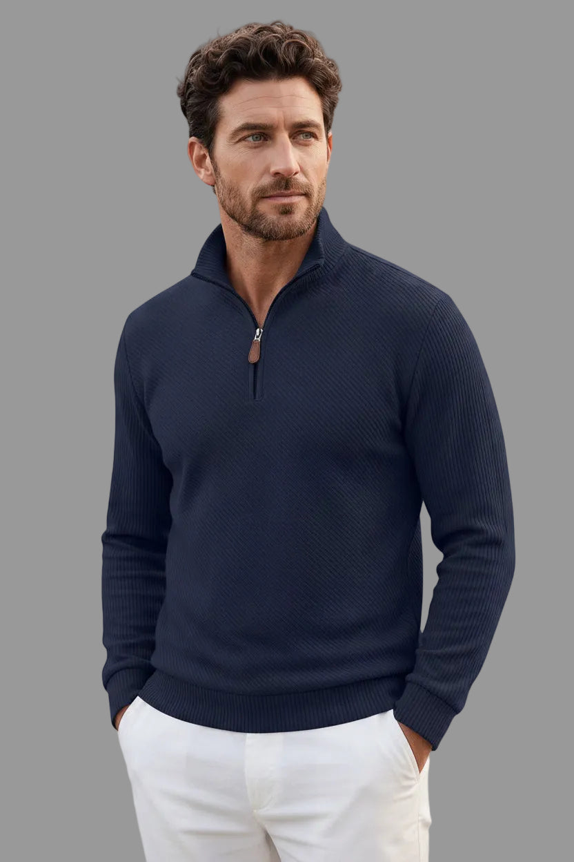 A man wearing a navy blue quarter-zip knit sweater with a subtle waffle texture, styled with white pants and black sunglasses against a plain white background.