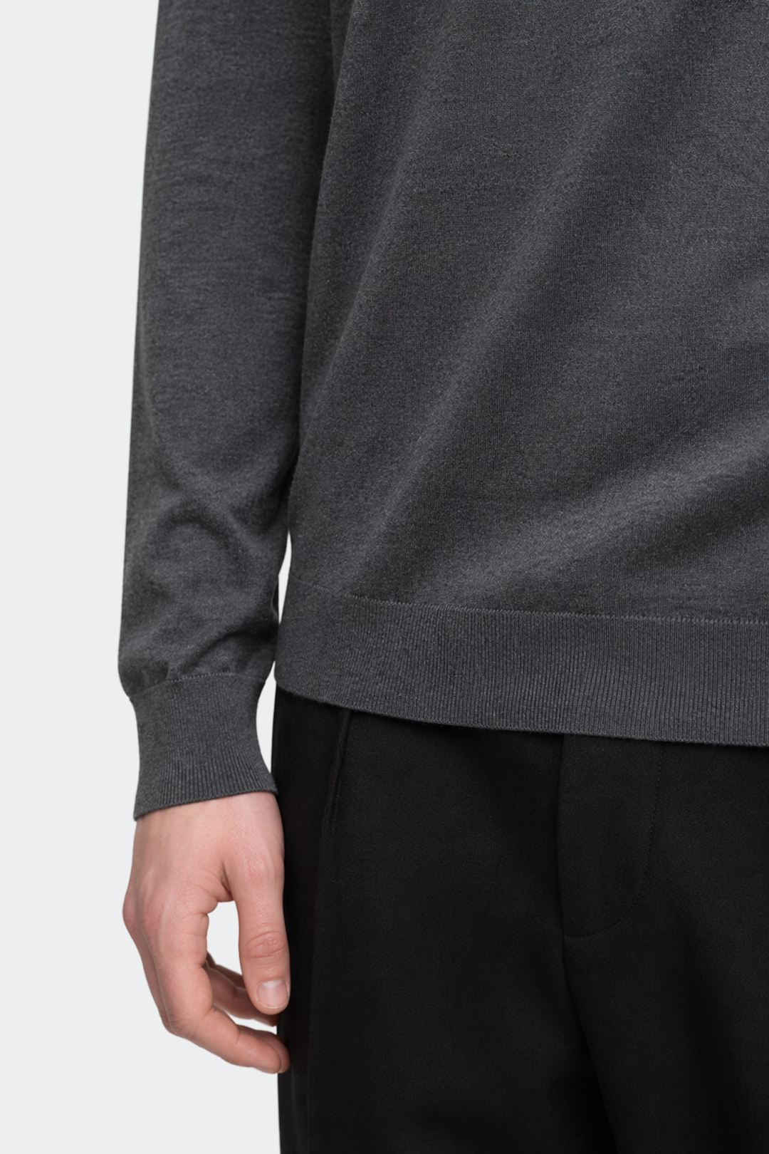Close-up of a person wearing a dark gray sweater and black pants on a white background
